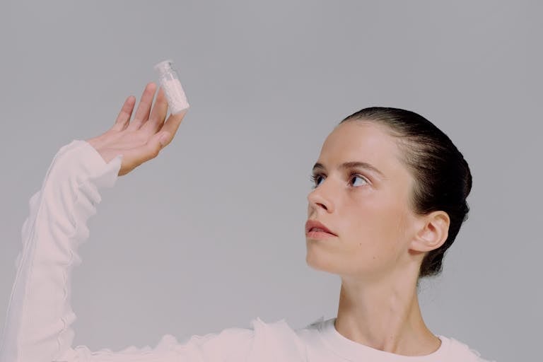 Portrait of a woman in a studio, holding and looking at a vial of pills with a contemplative expression.