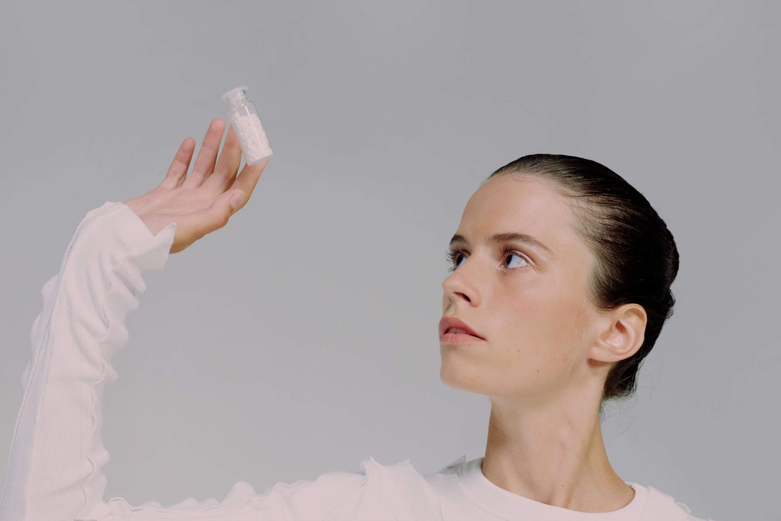 Portrait of a woman in a studio, holding and looking at a vial of pills with a contemplative expression.